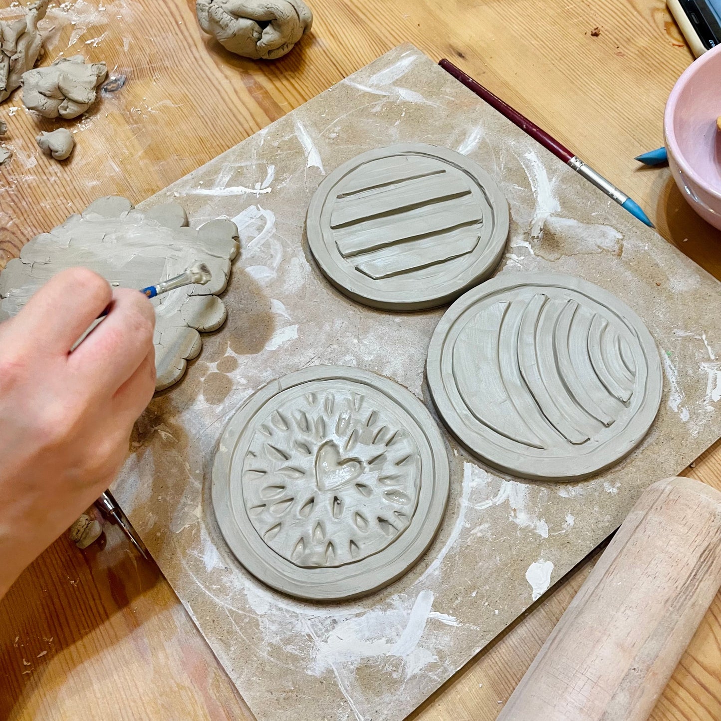 Clay stamp designs on a wooden table with a hand holding a tool.