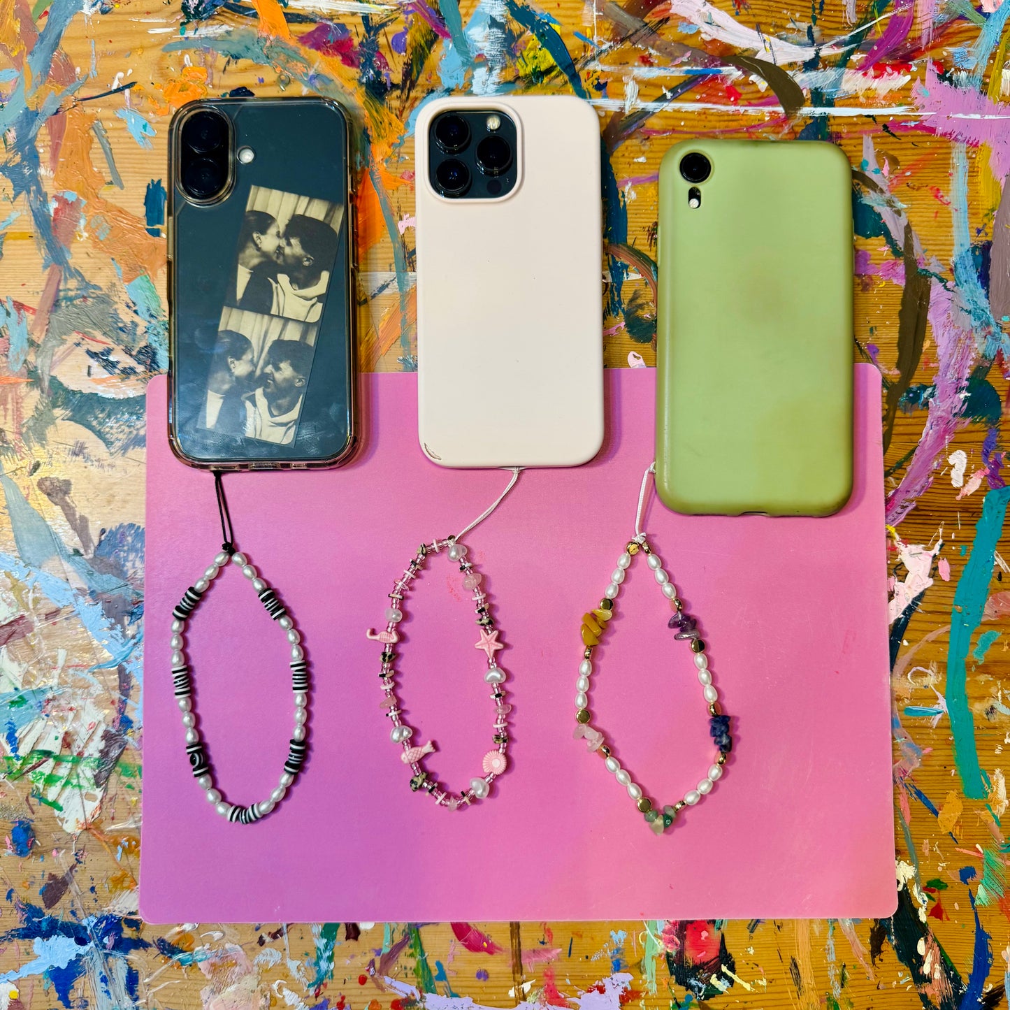 Three smartphones with colorful phone cases and beaded phone charms on a multicolored background