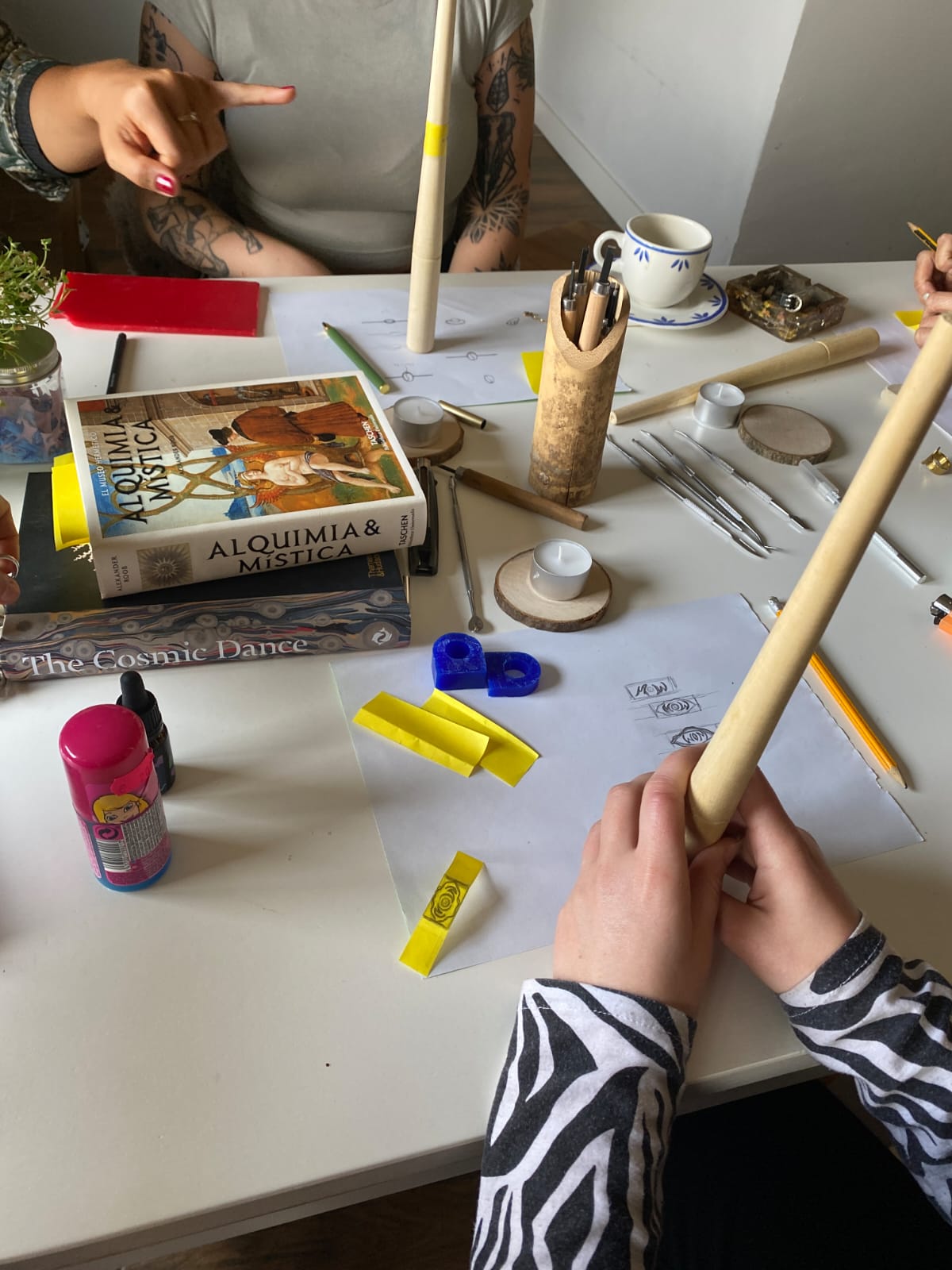 Person holding a wooden rod on a table with various items including a book and tools.