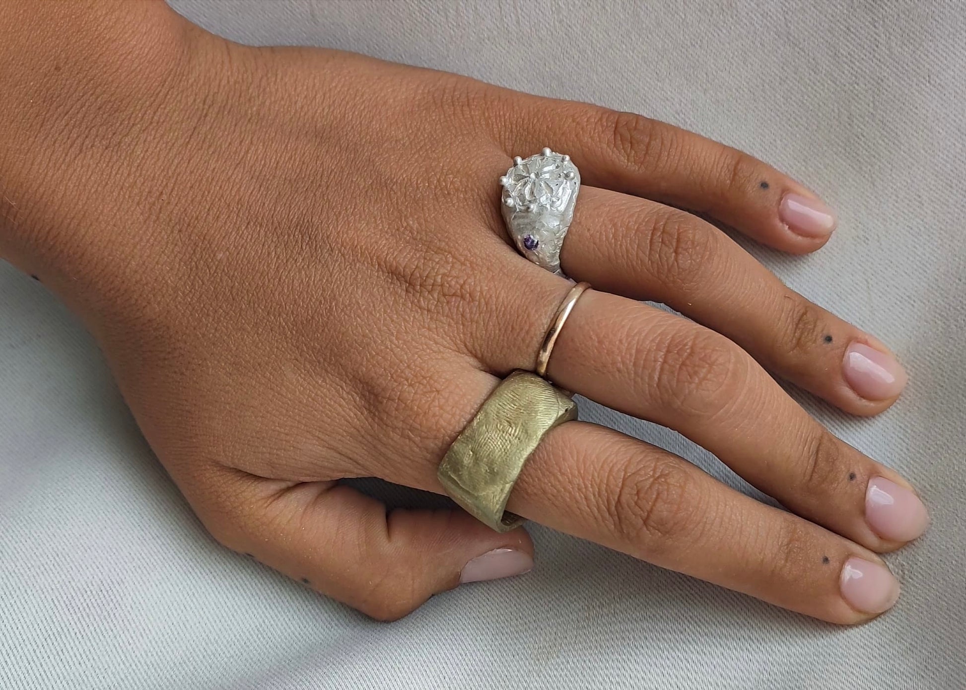 Hand wearing two rings on a neutral background