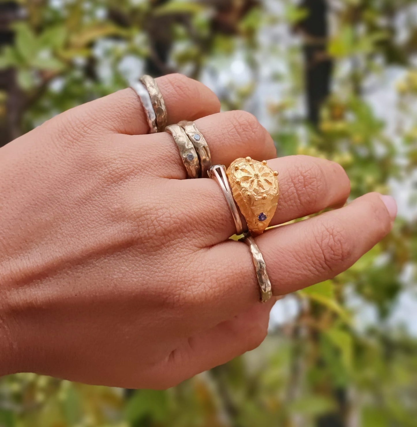 Hand wearing multiple gold and silver rings with a blurred natural background