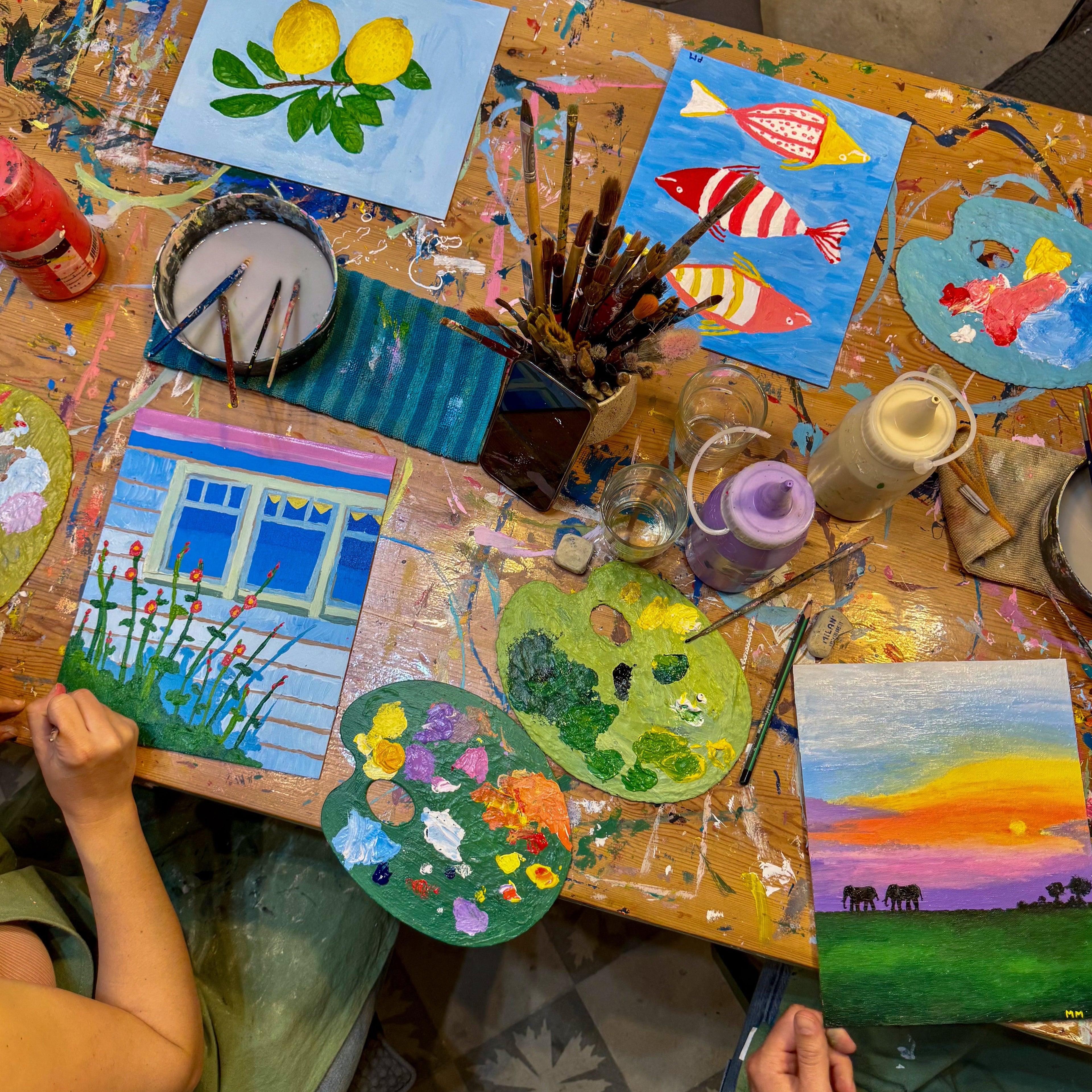 Canvasas with various colorful paintings and art supplies on a table.