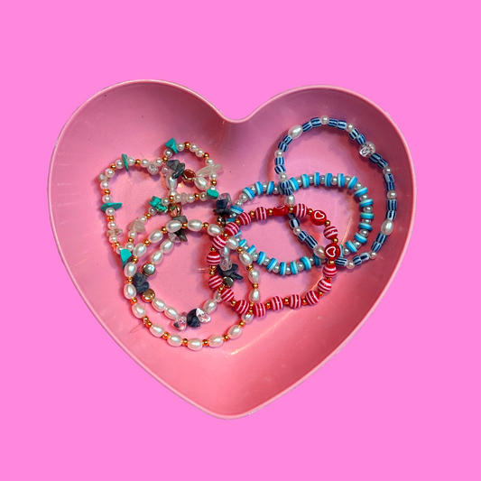 Heart-shaped pink dish with colorful beaded necklaces on a pink background